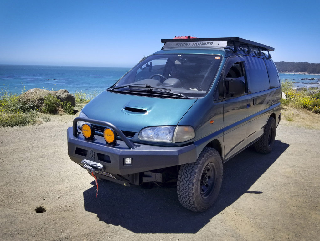 A black Front Runner platform roof rack sits on a teal-colored Mitsubishi Delica Space Gear